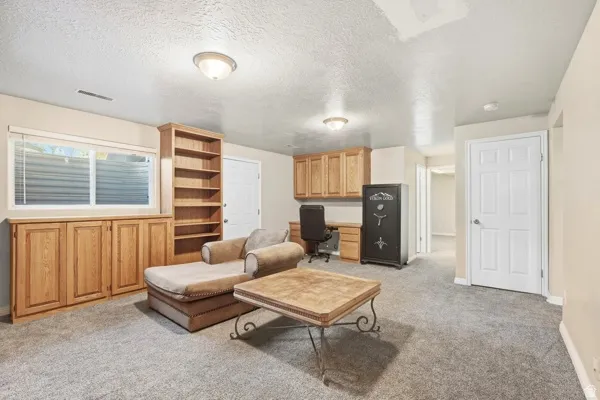 Recessed window with built-in wood cabinetry, integrated wood shelving, built-in wood desk with overhead wood cabinetry, and neutral carpeting