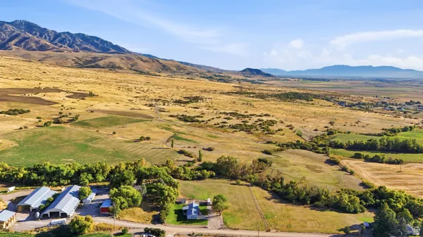 Expansive rural property featuring multiple outbuildings, a detached residence, and agricultural fields, set against a mountainous backdrop