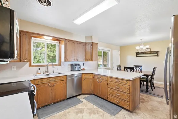 Kitchen featuring wood cabinetry, light-toned countertops, tile flooring, and a stainless steel dishwasher