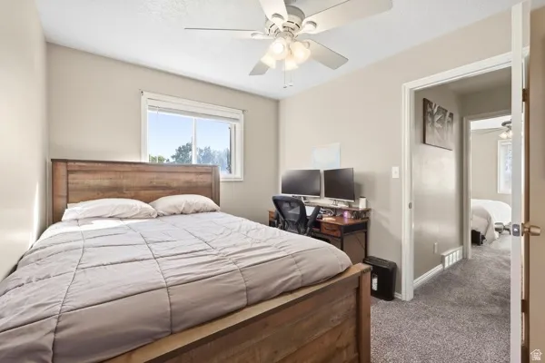 Carpeted room featuring a ceiling fan with integrated lighting, a window, and a wooden bed frame