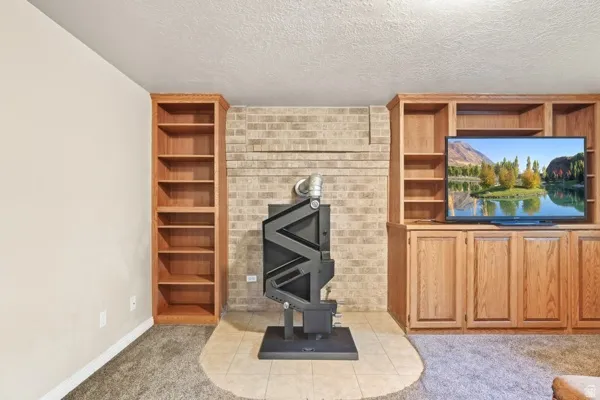 Built-in cabinetry with open shelving, integrated media center, brick-finish wall detail, and a tile hearth with a freestanding stove