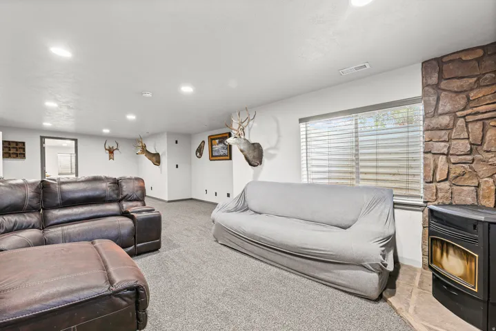 Recessed lighting, light gray carpeting, stone-clad accent wall, window with blinds, and built-in stove fireplace