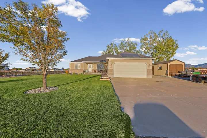 Single-story residence featuring a two-car garage, solar panels, a detached shed, a concrete driveway, and a fenced backyard with mature trees