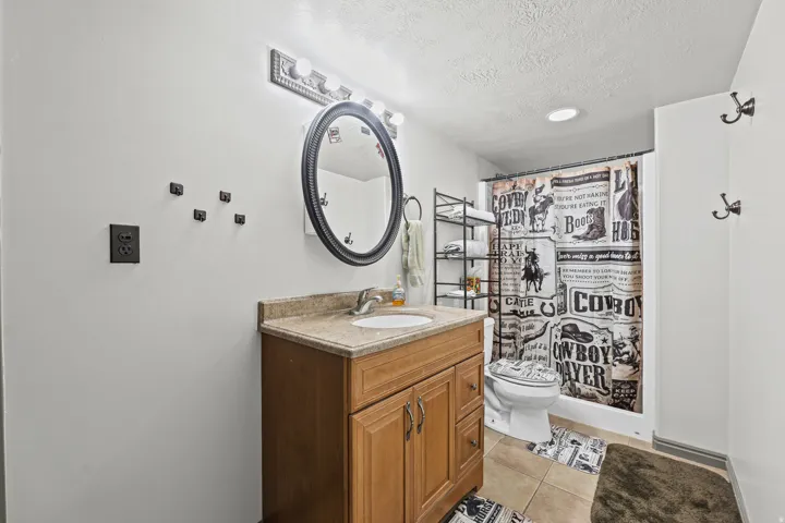 Vanity with a light wood-finish cabinet and stone countertop, undermount sink, and oval framed mirror