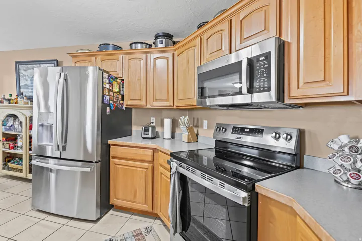 Stainless steel appliances, wood-finish cabinetry, light-toned countertops, and tiled flooring