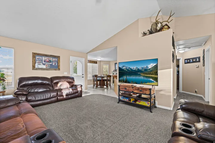 Vaulted ceiling, neutral wall tones, carpeted flooring, window with blinds, and white interior door with an arched glass insert