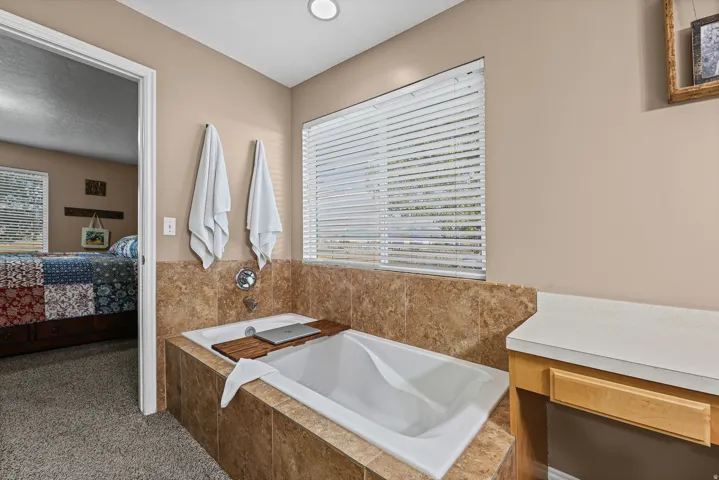 Built-in soaking tub with a tiled surround, integrated wall-mounted faucet, and a large window with blinds