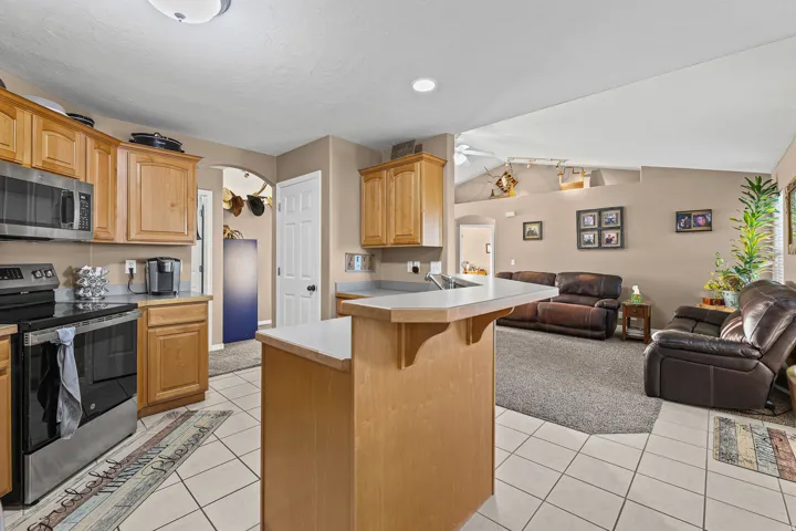Kitchen featuring wood cabinetry, stainless steel appliances, and a breakfast bar, with tile flooring extending into an open living area