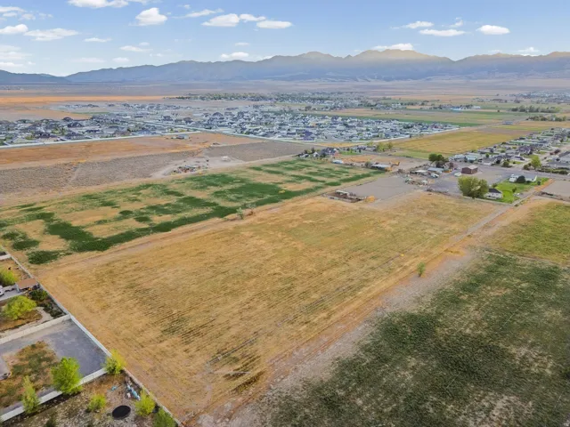 Expansive land parcel featuring natural ground cover, surrounded by residential areas and distant mountains