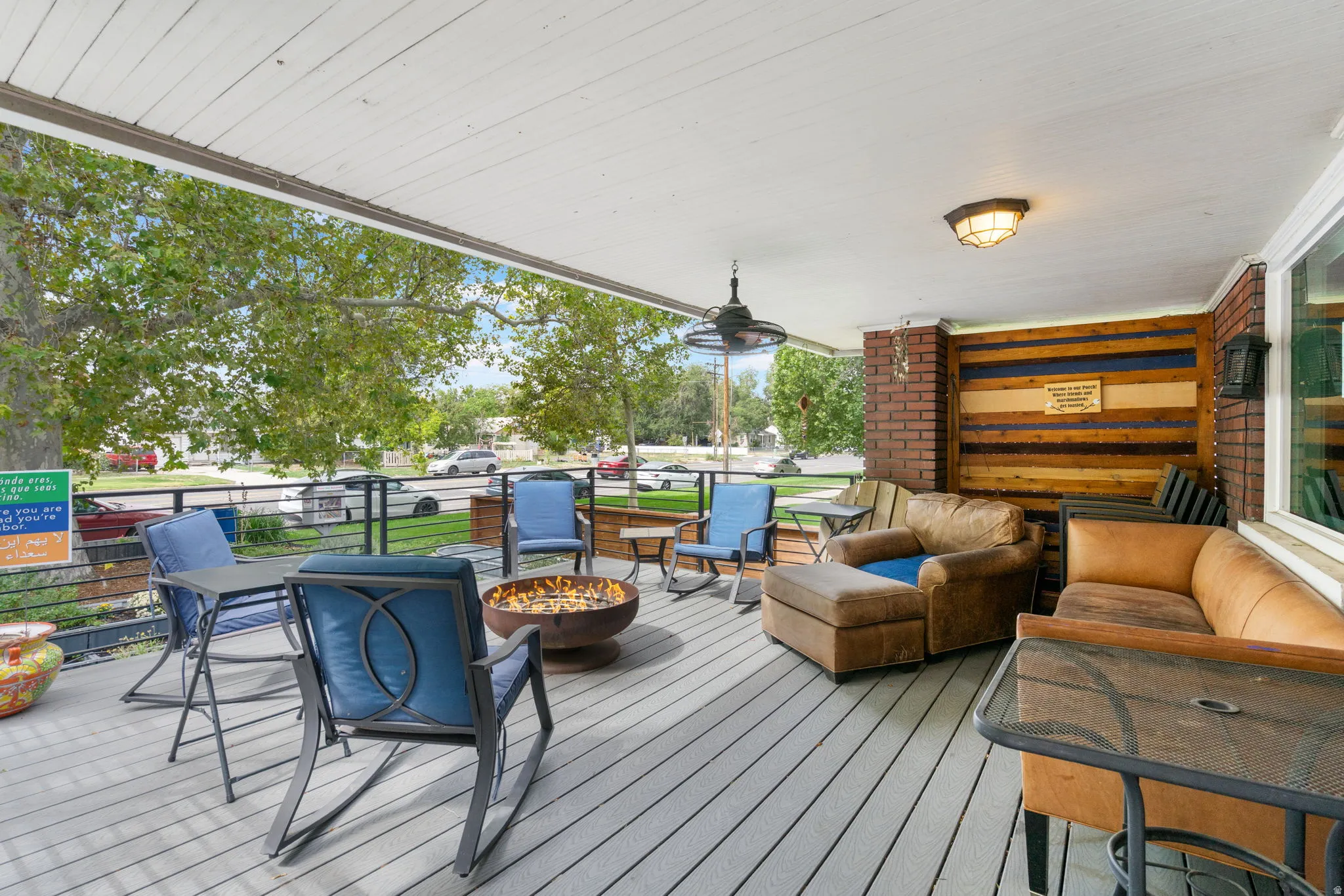 Covered front porch with composite decking, brick columns, wood-paneled accent wall, and ceiling fan