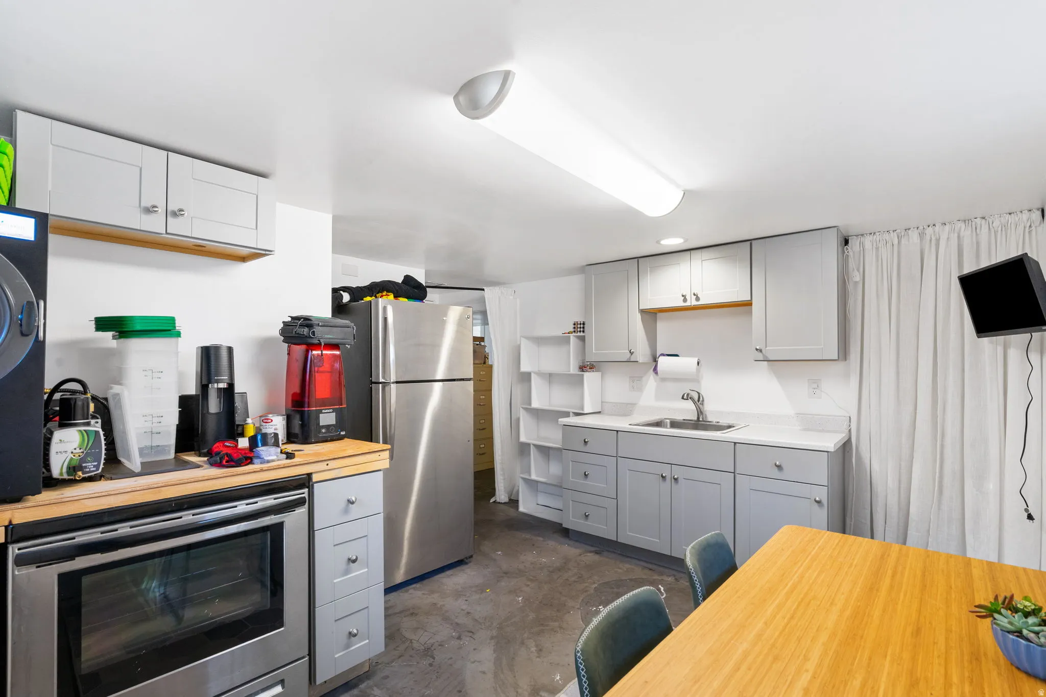Gray shaker cabinetry, stainless steel oven, stainless steel refrigerator, white countertops, and a stainless steel sink
