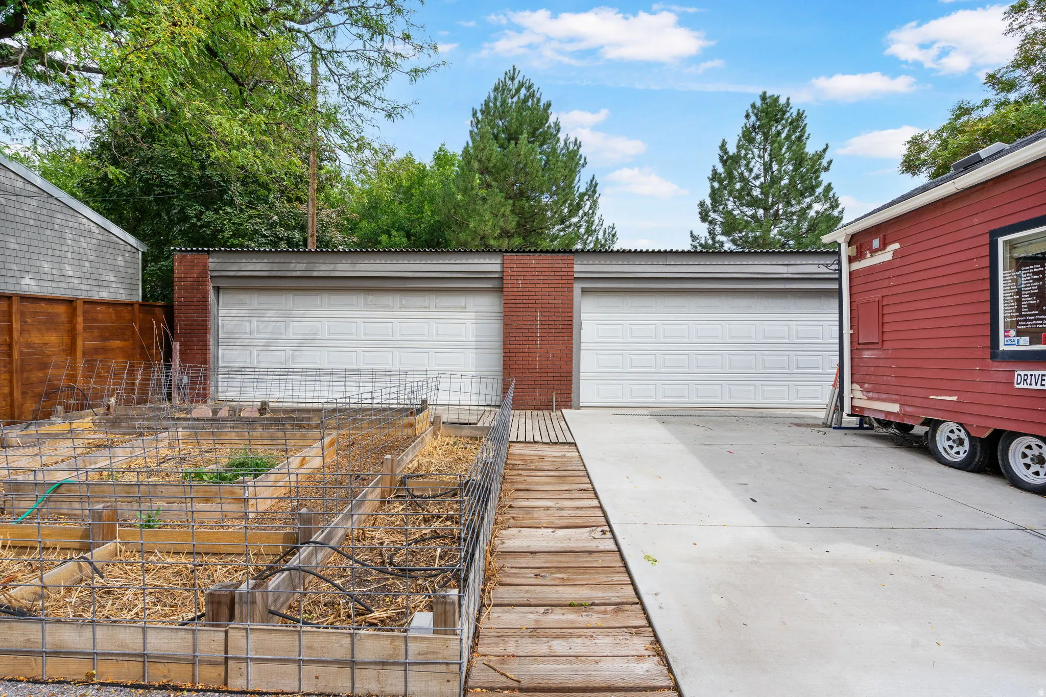 Two-car garage with brick accents, concrete driveway, and raised garden beds