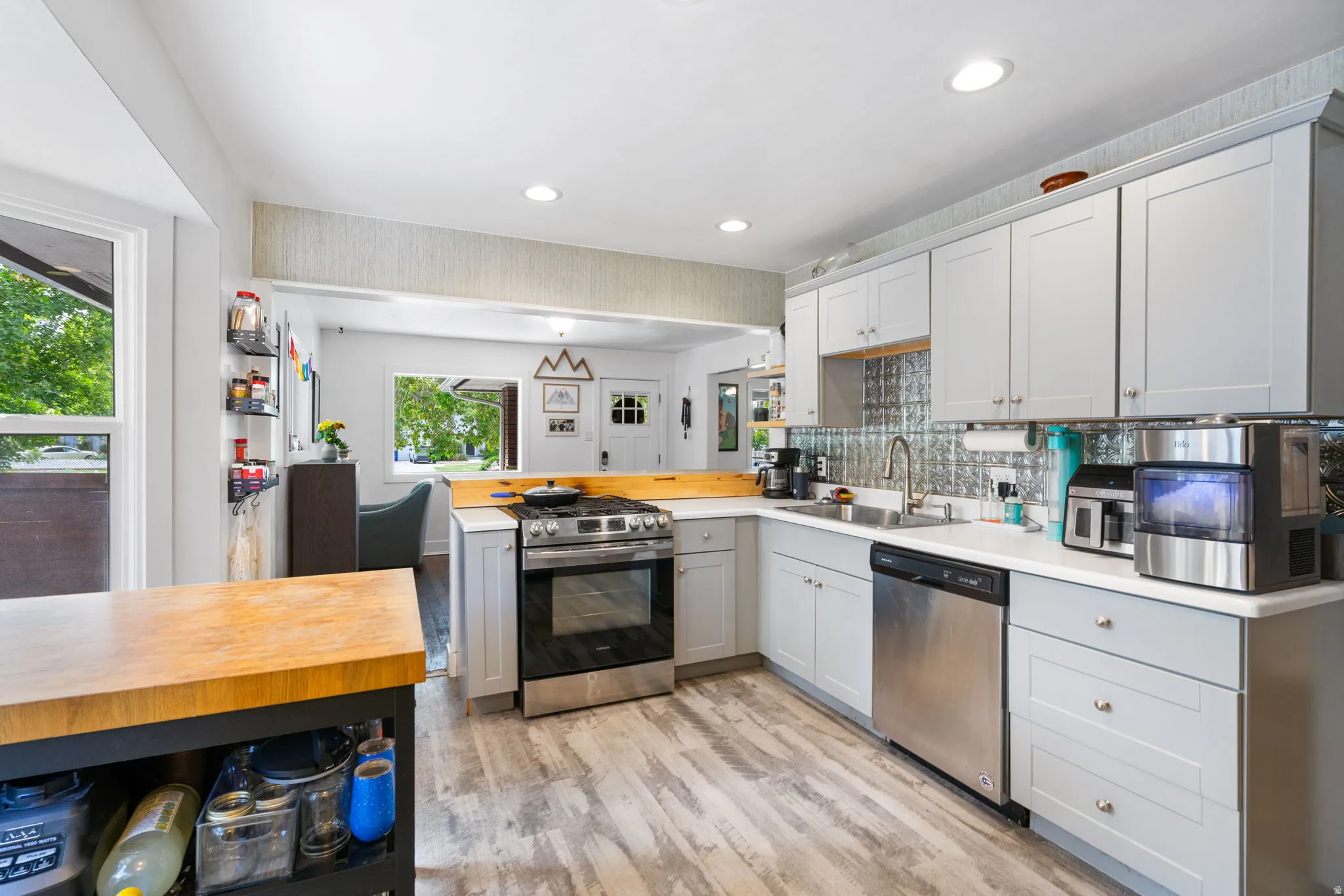 Light gray cabinetry with brushed nickel hardware, stainless steel appliances, wood-finish flooring, white countertops, and a textured backsplash