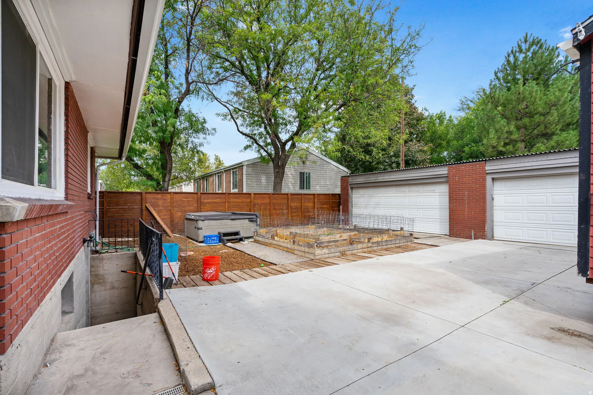 Concrete patio area with a privacy fence, two garage doors, and a built-in planter