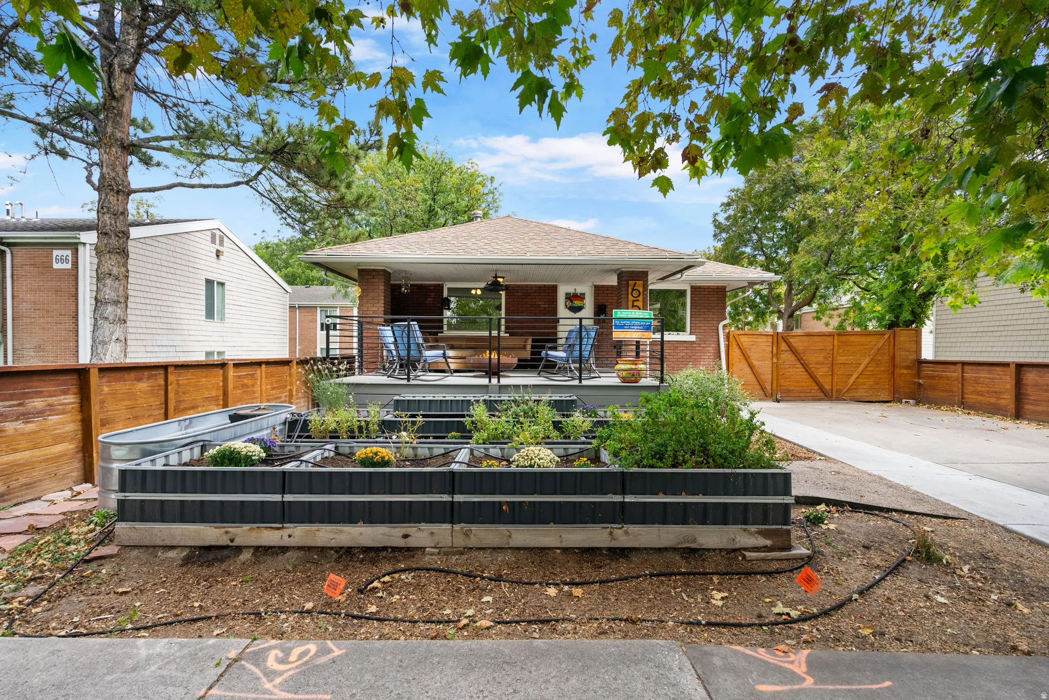 Brick exterior, covered front porch, tiered front garden beds, wood fencing, and concrete driveway