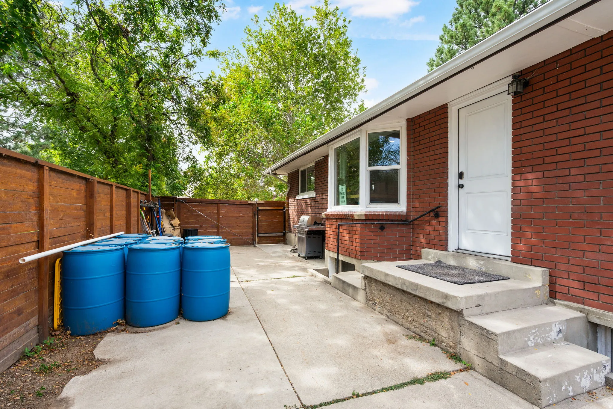 Red brick exterior, concrete patio, concrete steps, wood privacy fence, and white-framed windows