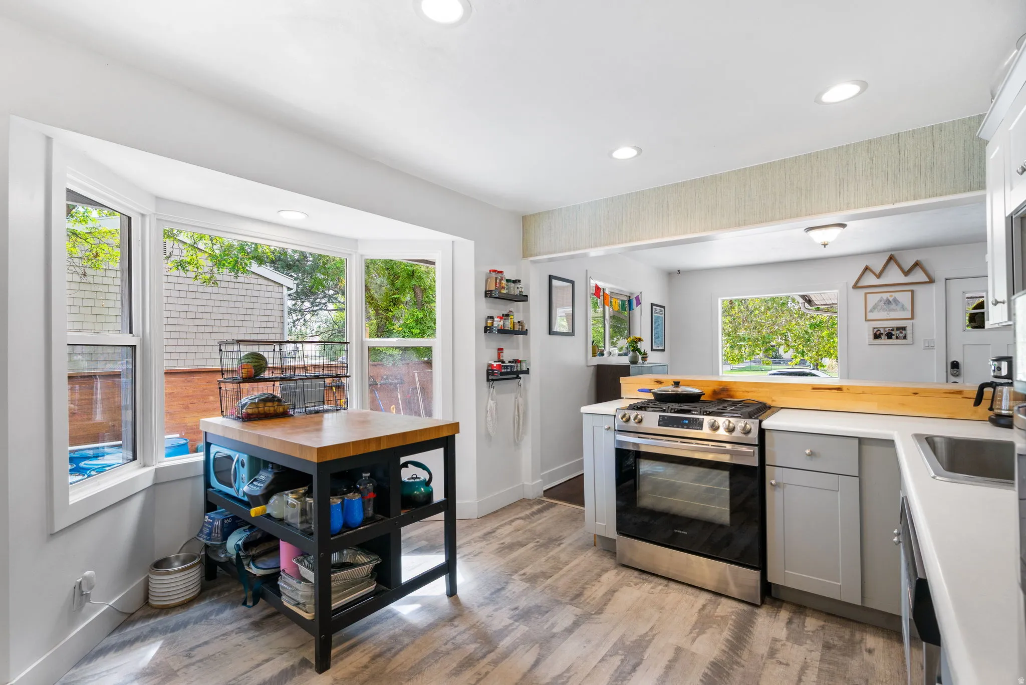 Kitchen featuring a stainless steel range, white countertops, light gray cabinetry, wood-finish flooring, and a bay window