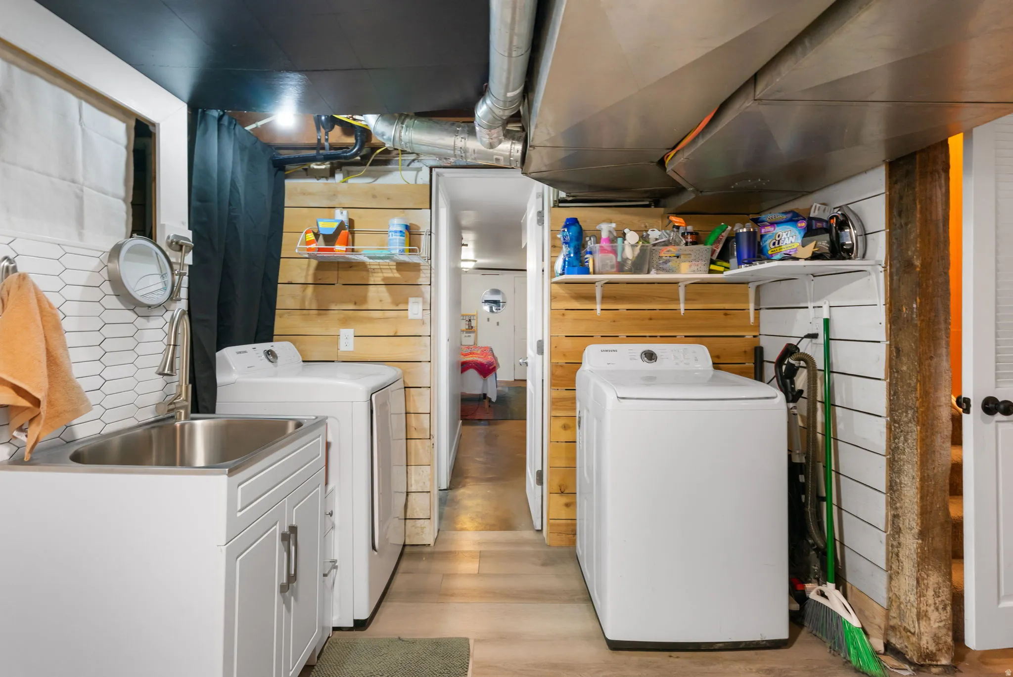 Utility space featuring a laundry area with a stainless steel sink, white cabinetry, and shiplap wall finishes