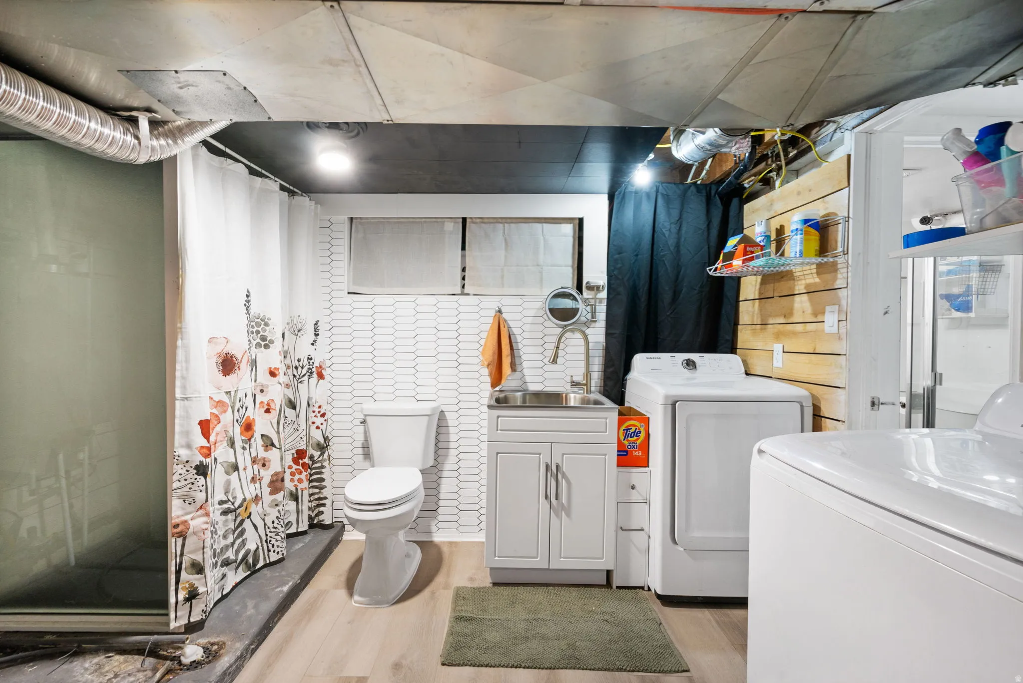 Wood-finish flooring, white vanity with integrated sink, white toilet, and white tile wall accents