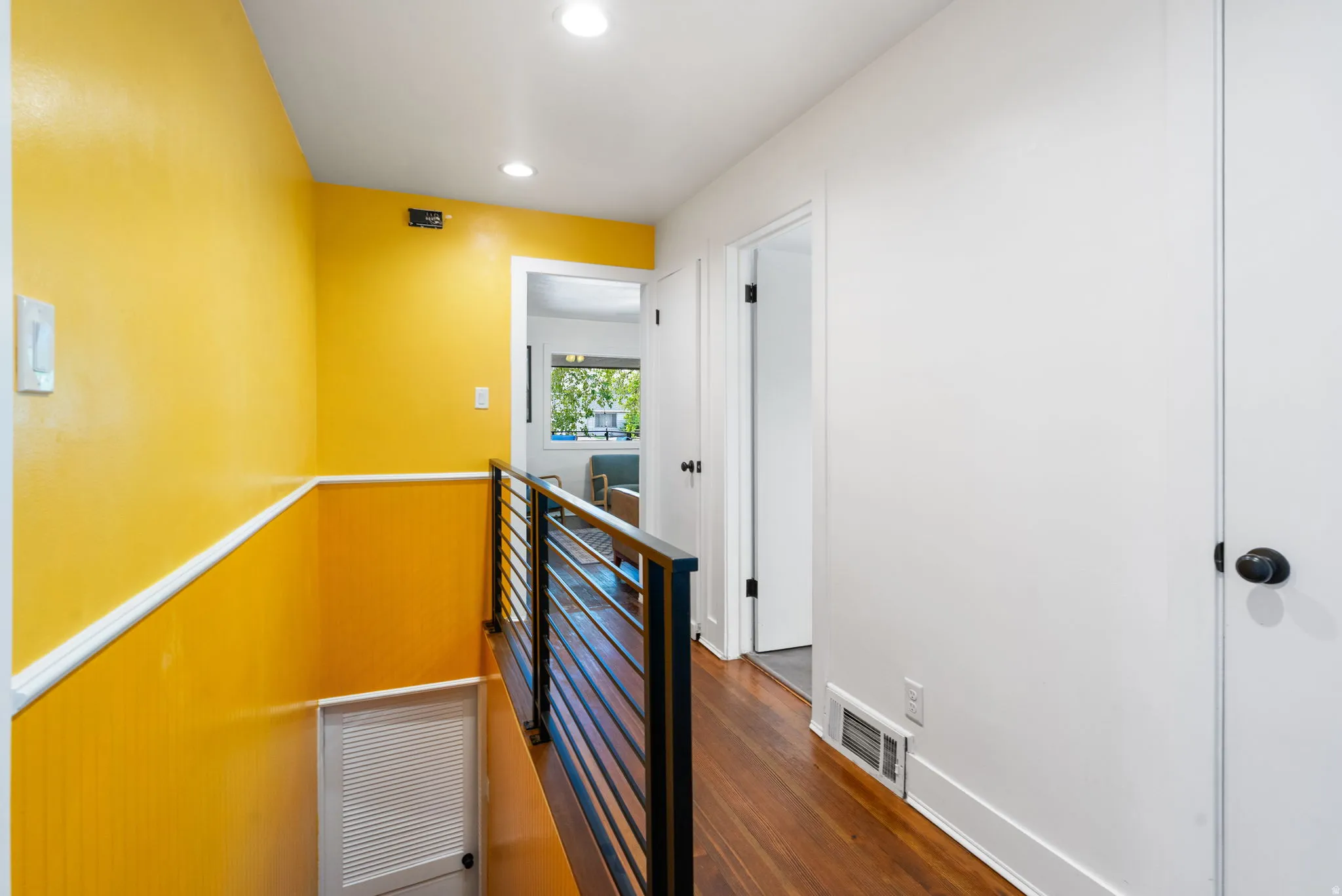 Hardwood flooring, painted walls, ceiling-mounted lighting, interior doors with matte black hardware, and a metal stair railing