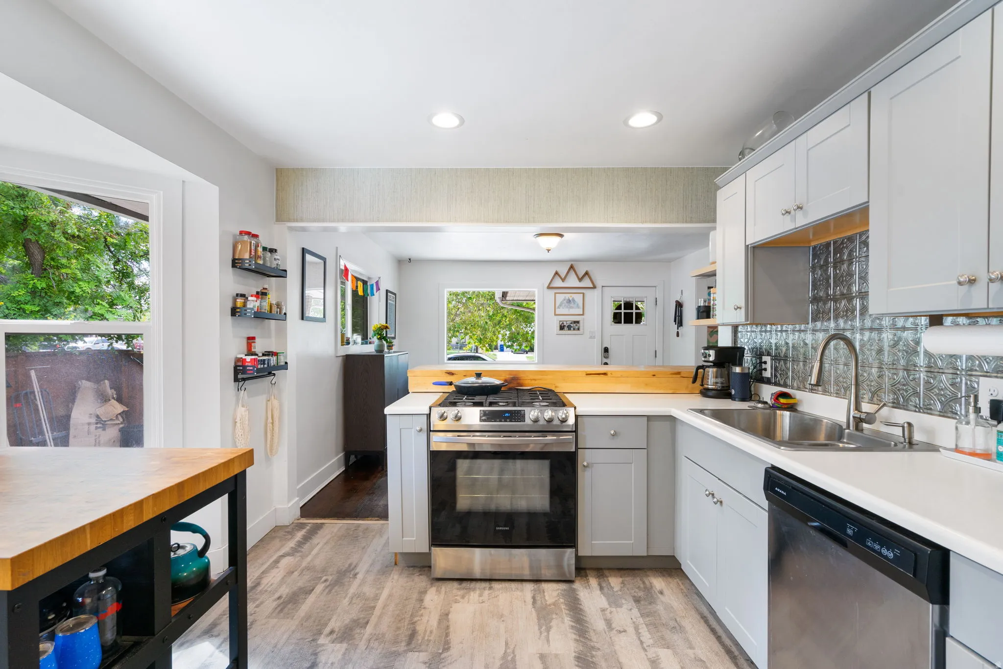White cabinetry with brushed nickel hardware, stainless steel gas range, stainless steel dishwasher, pressed tin backsplash, and wood-finish flooring