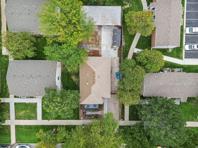 Aerial property overview featuring a shingle roof, concrete drive, and mature trees
