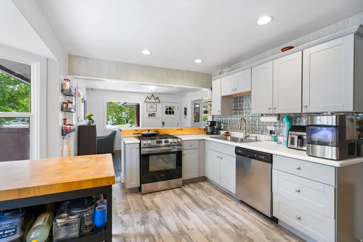Light gray cabinetry with brushed nickel hardware, stainless steel appliances, wood-finish flooring, white countertops, and a textured backsplash
