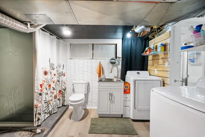 Wood-finish flooring, white vanity with integrated sink, white toilet, and white tile wall accents
