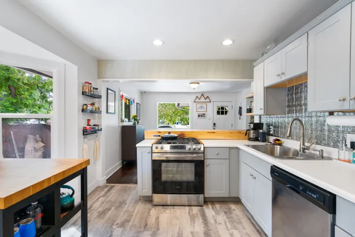 White cabinetry with brushed nickel hardware, stainless steel gas range, stainless steel dishwasher, pressed tin backsplash, and wood-finish flooring