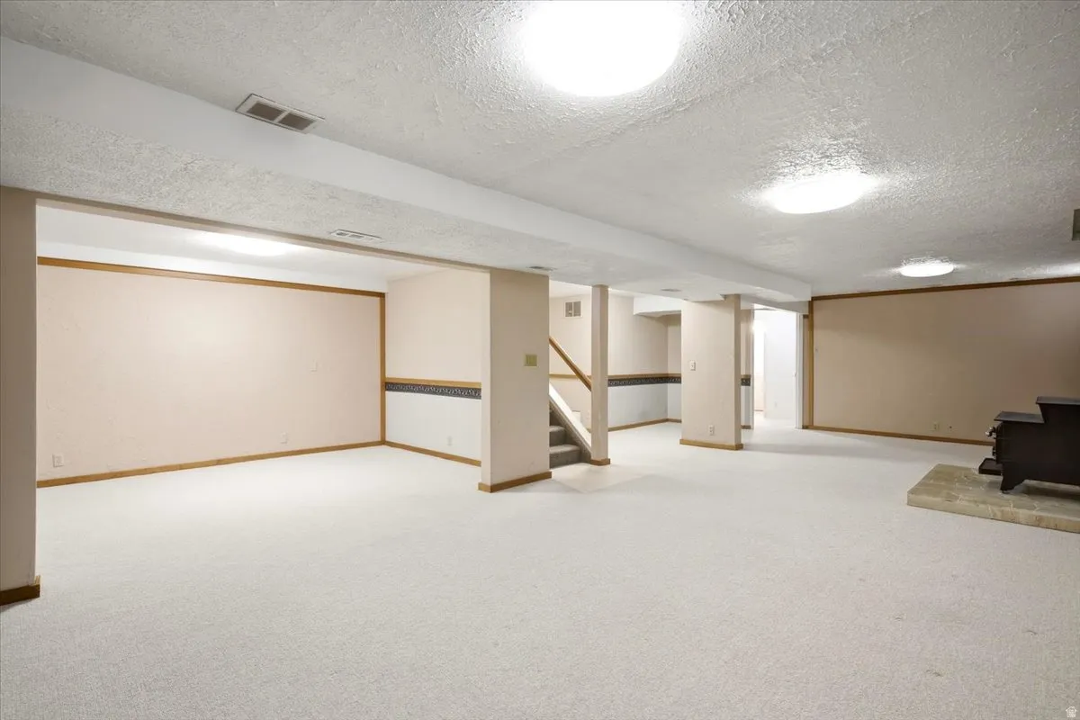 Expansive finished lower level featuring carpet flooring, recessed lighting, support columns, and a built-in wood stove on a stone hearth