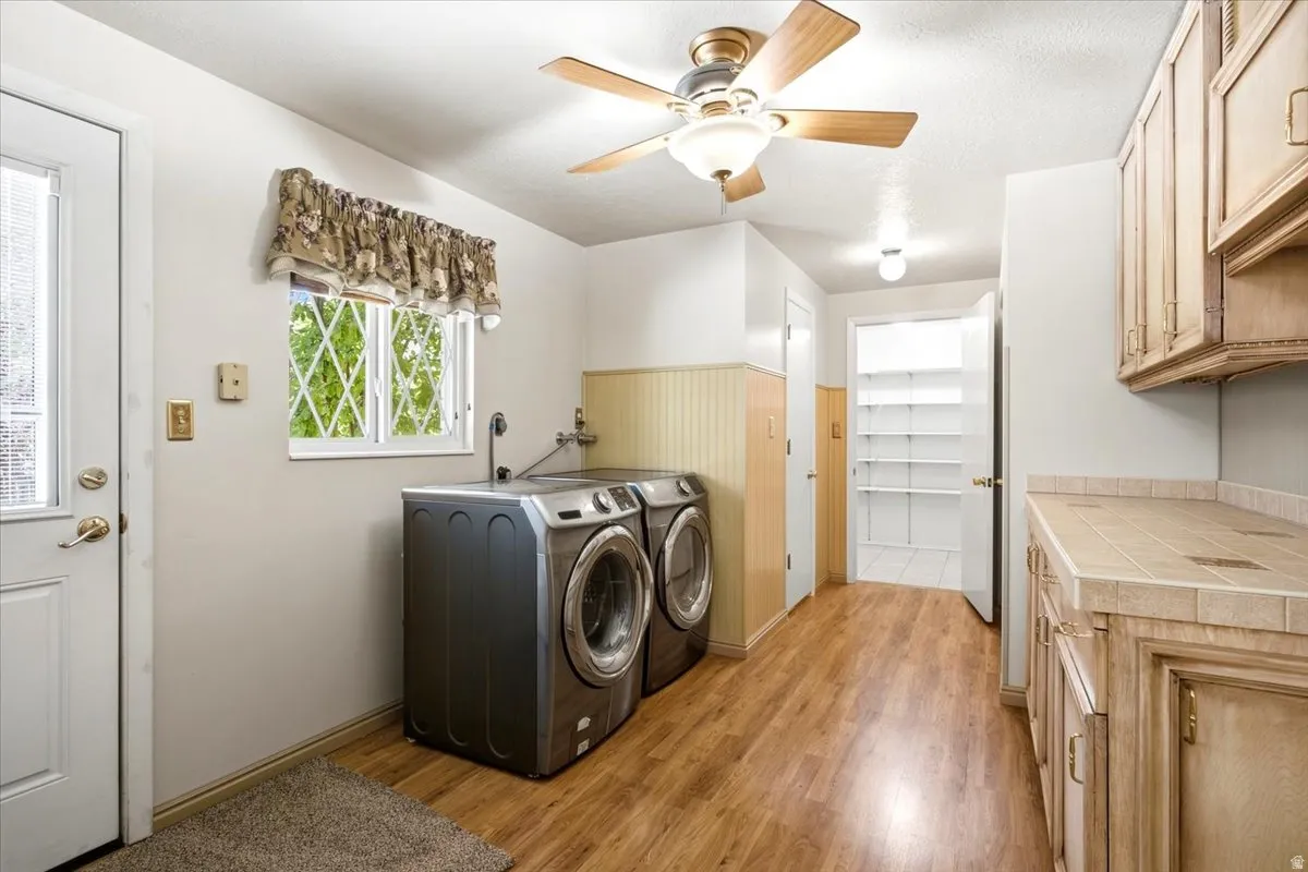 Wood-finish flooring, overhead ceiling fan with lighting, built-in shelving, tile countertop, and cabinetry with brass hardware