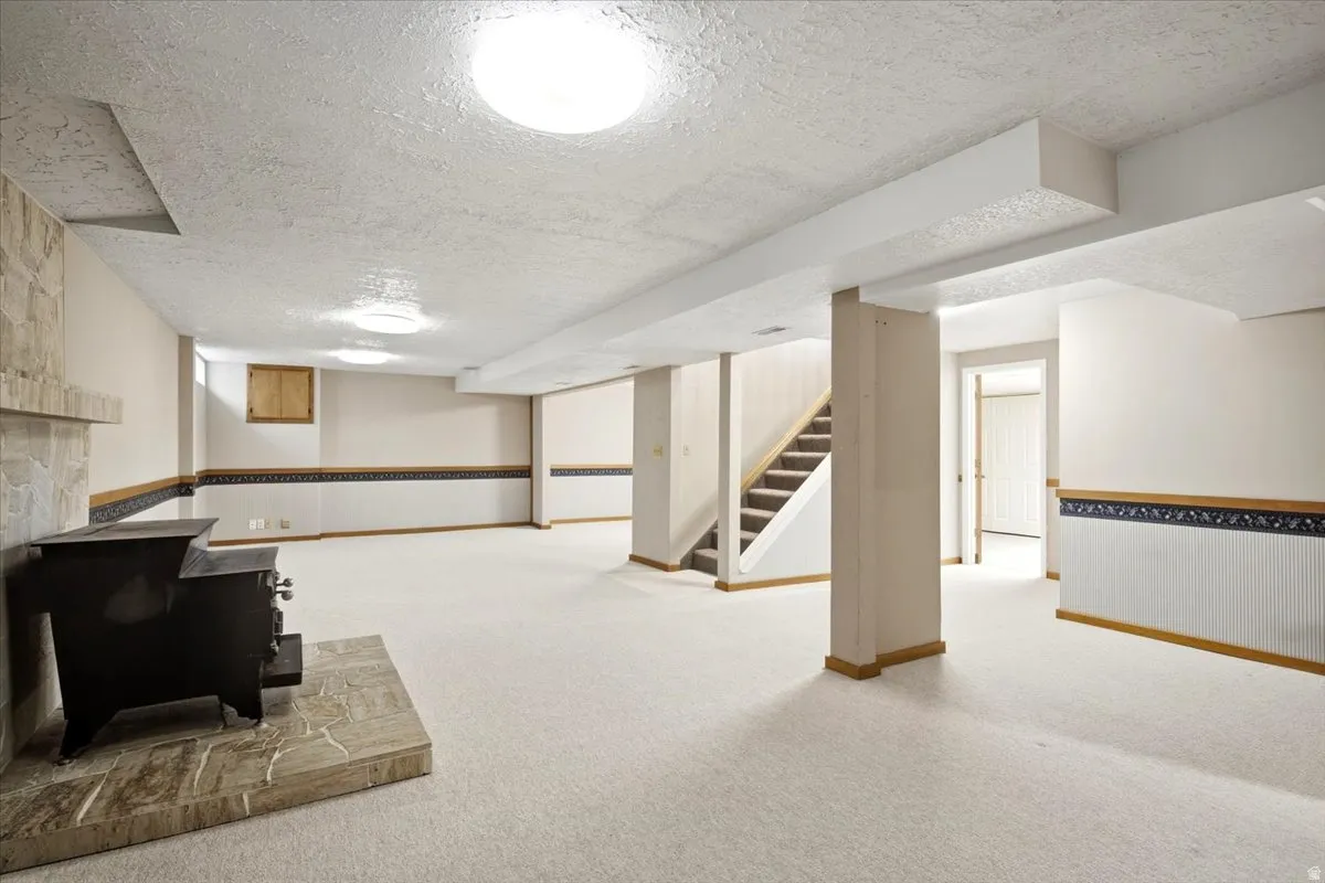 Expansive carpeted room featuring a stone fireplace with a wood-burning stove, recessed lighting, and a staircase