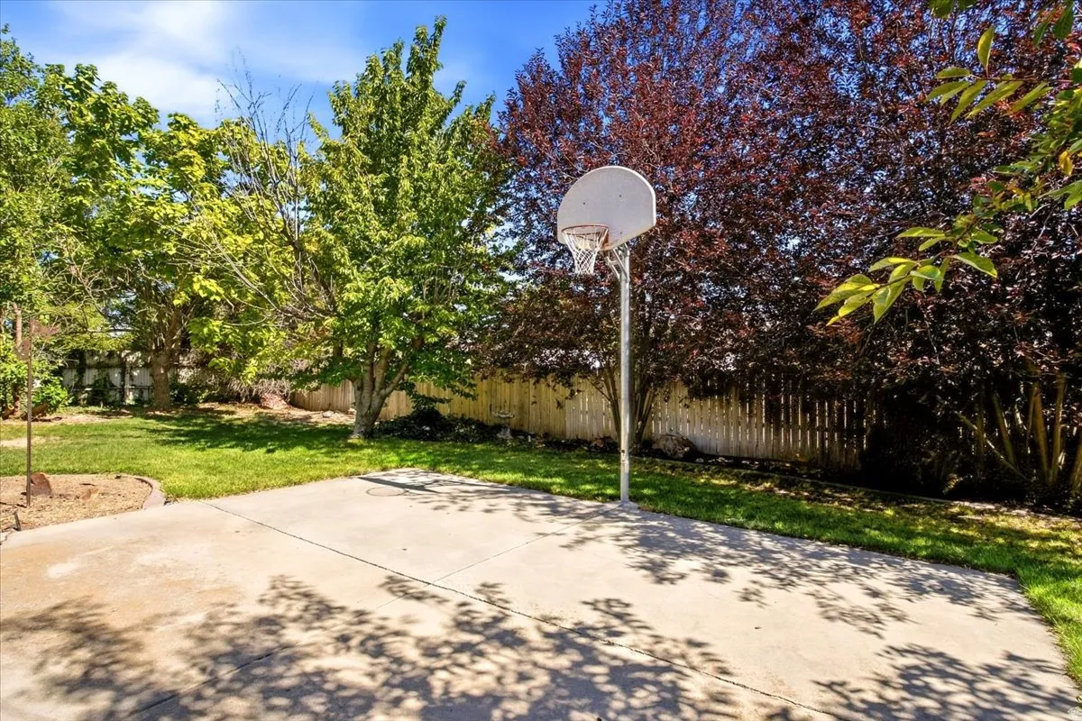 Expansive concrete pad, lush green lawn, mature trees, and privacy fencing