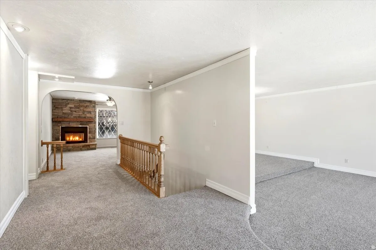 Stone-faced fireplace, arched entryway, light-toned carpeting, wood railing, and white interior walls