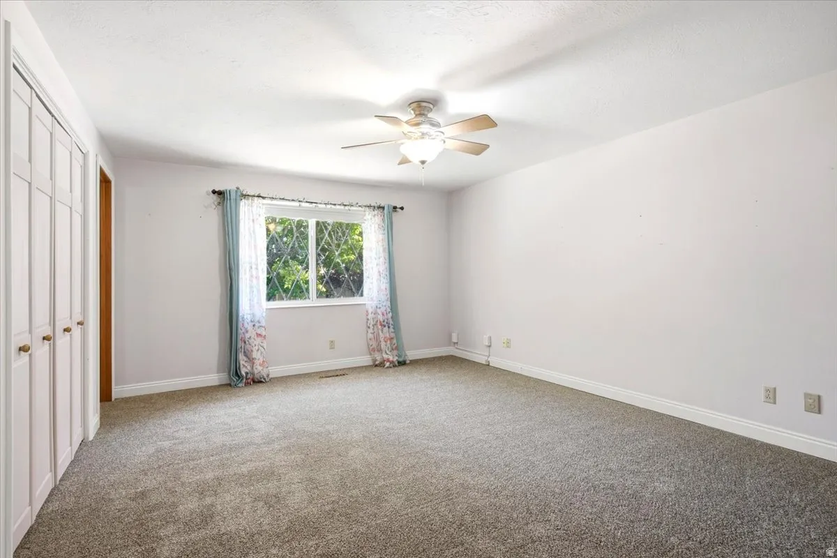 Spacious room with plush carpeting, a multi-pane window, and a ceiling fan with integrated lighting