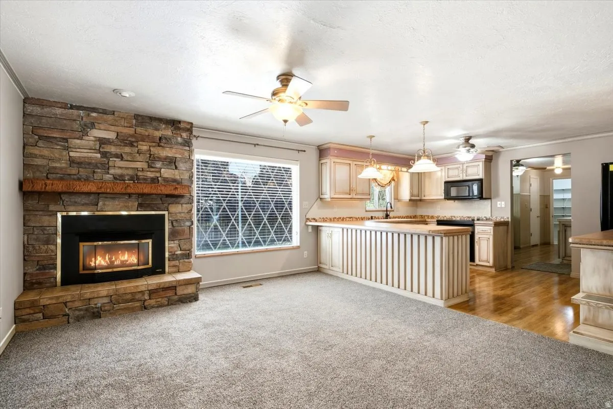 Stone-clad fireplace with wood mantel, large window with blinds, kitchen with built-in cabinetry, range, and microwave, and wood-finish flooring