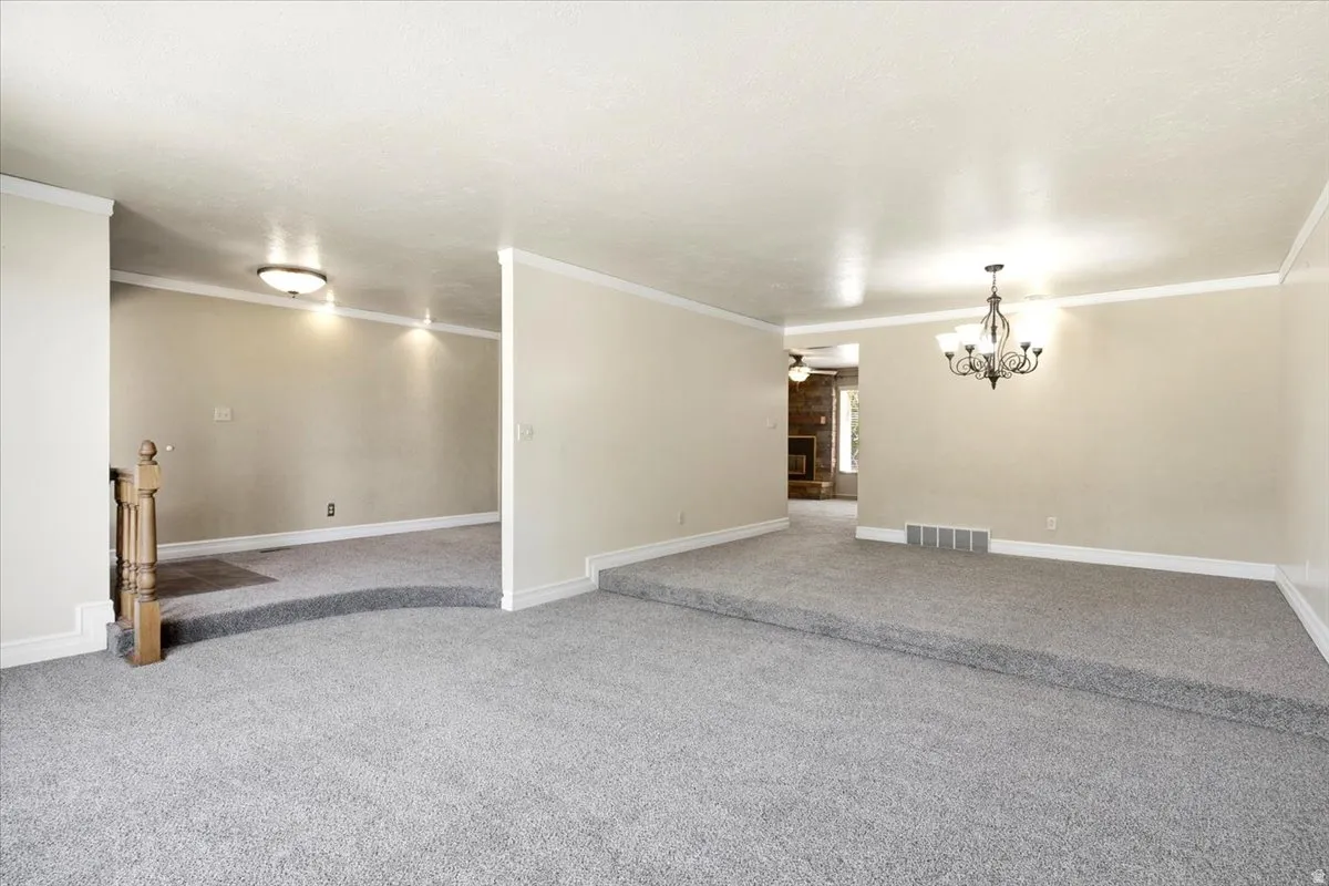 Multi-level interior space featuring neutral carpeting, crown molding, a decorative chandelier, and recessed lighting