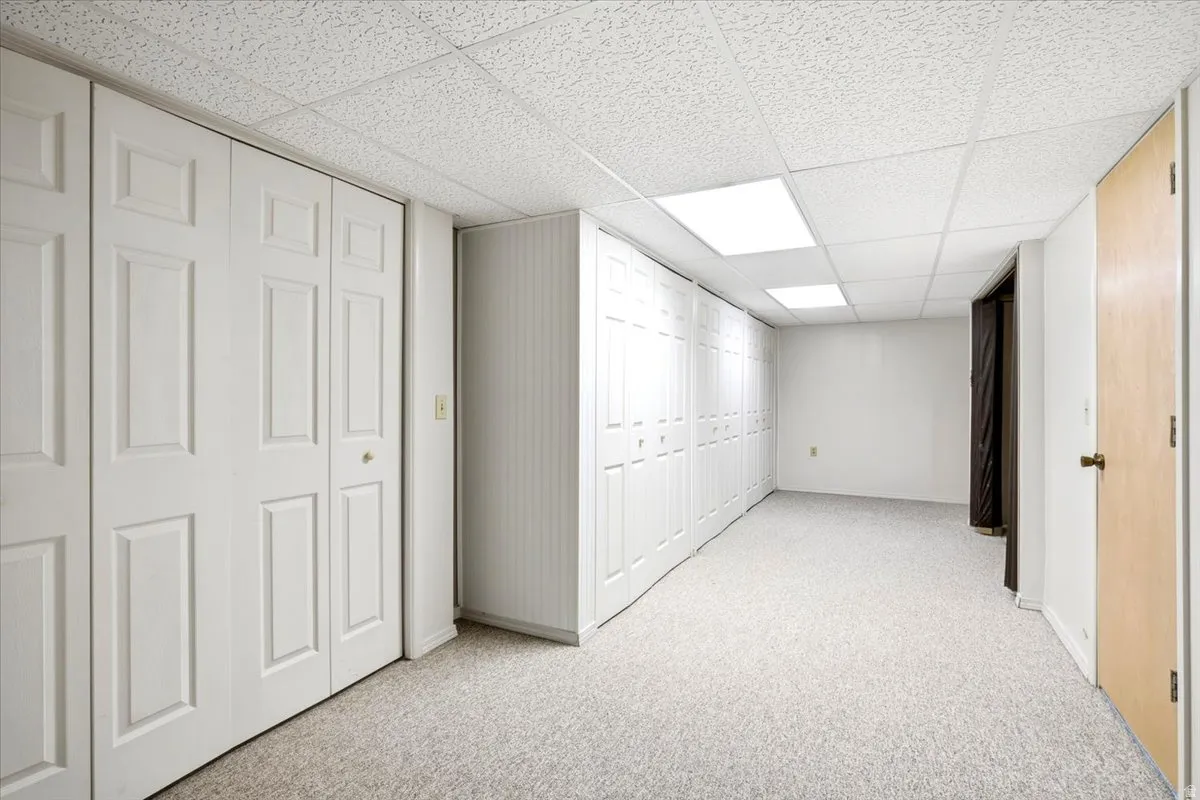 Room featuring wall-to-wall carpeting, extensive bi-fold closet doors, a drop ceiling with recessed lighting, and a light wood-finish door