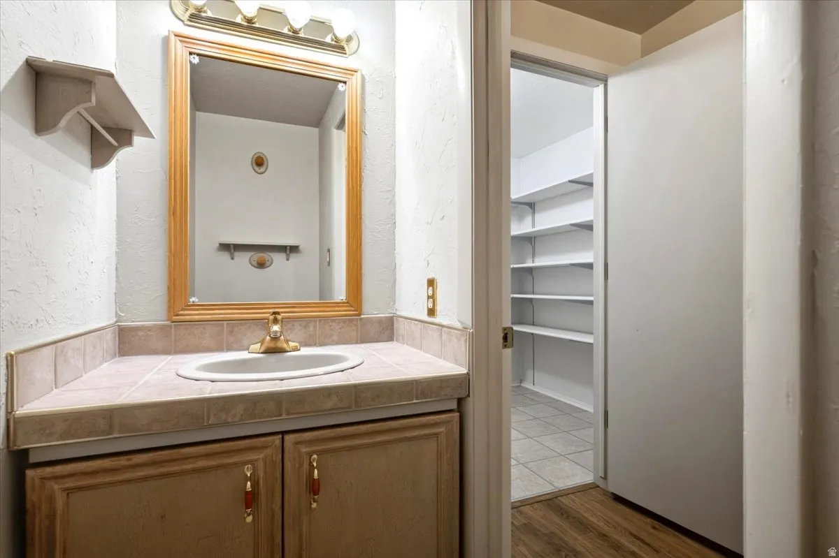 Vanity with a tiled countertop, undermount sink, and wood-finish cabinetry