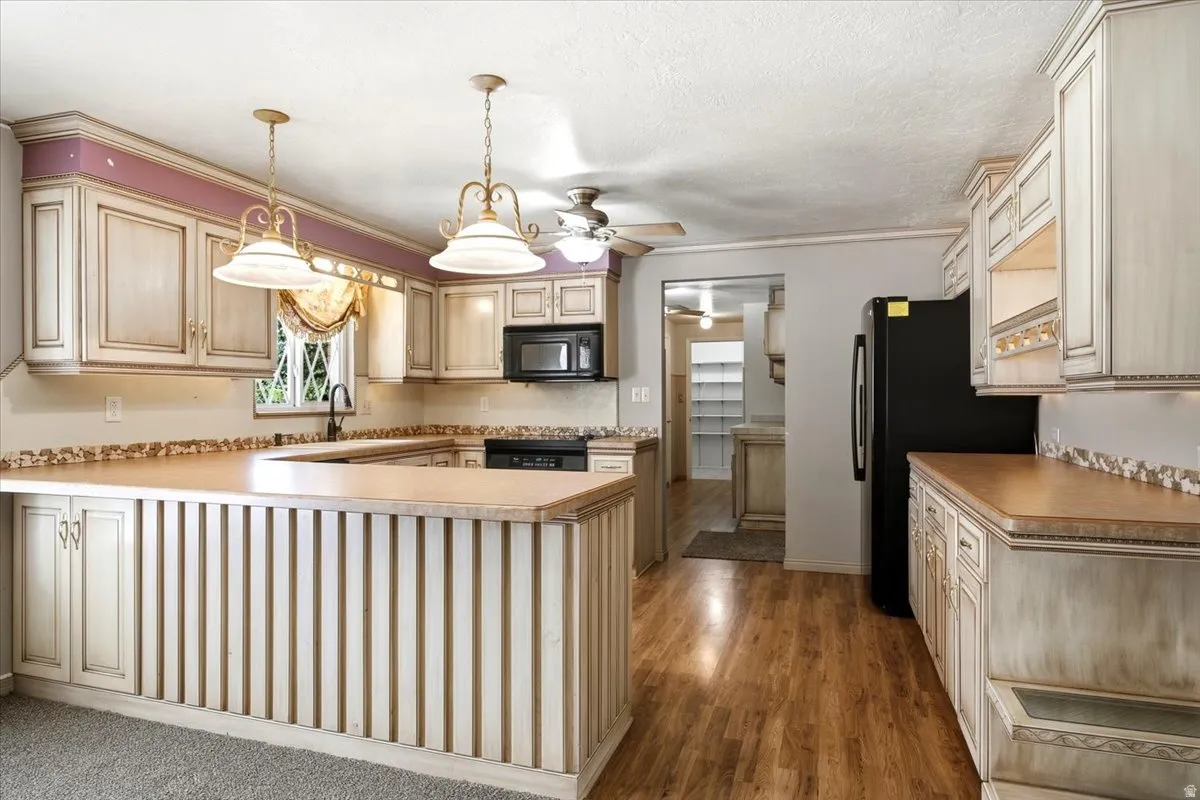 Expansive kitchen featuring wood-finish flooring, custom cabinetry with ornate details, black built-in appliances, and a breakfast bar