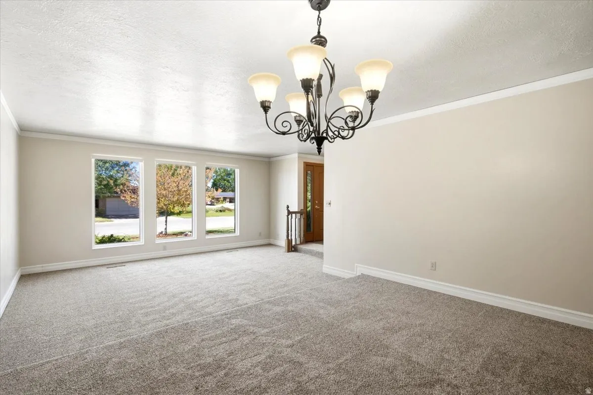 Textured ceiling, crown molding, white trim, multiple pane windows, and a decorative chandelier