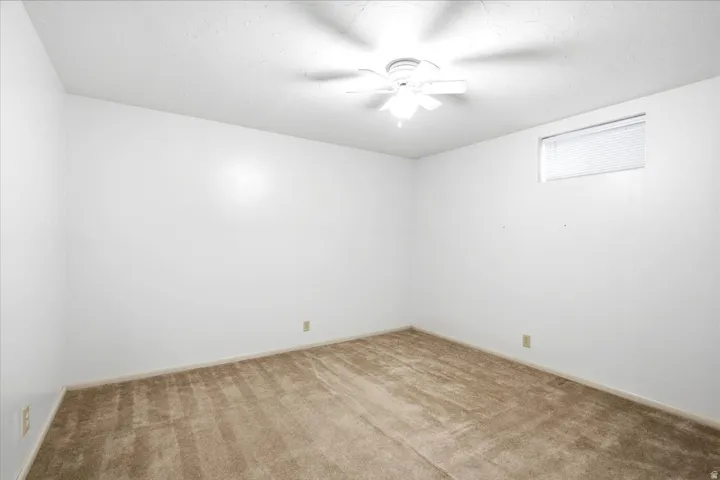 Neutral white walls, plush carpet, ceiling fan, and a transom window