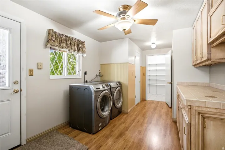 Wood-finish flooring, overhead ceiling fan with lighting, built-in shelving, tile countertop, and cabinetry with brass hardware