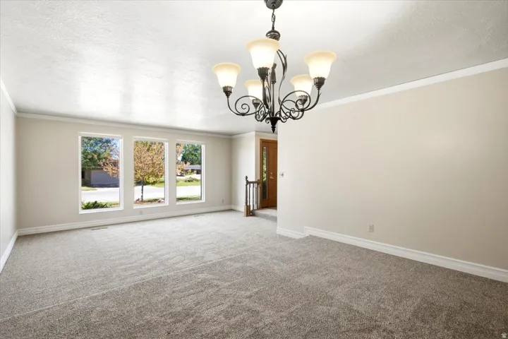 Textured ceiling, crown molding, white trim, multiple pane windows, and a decorative chandelier