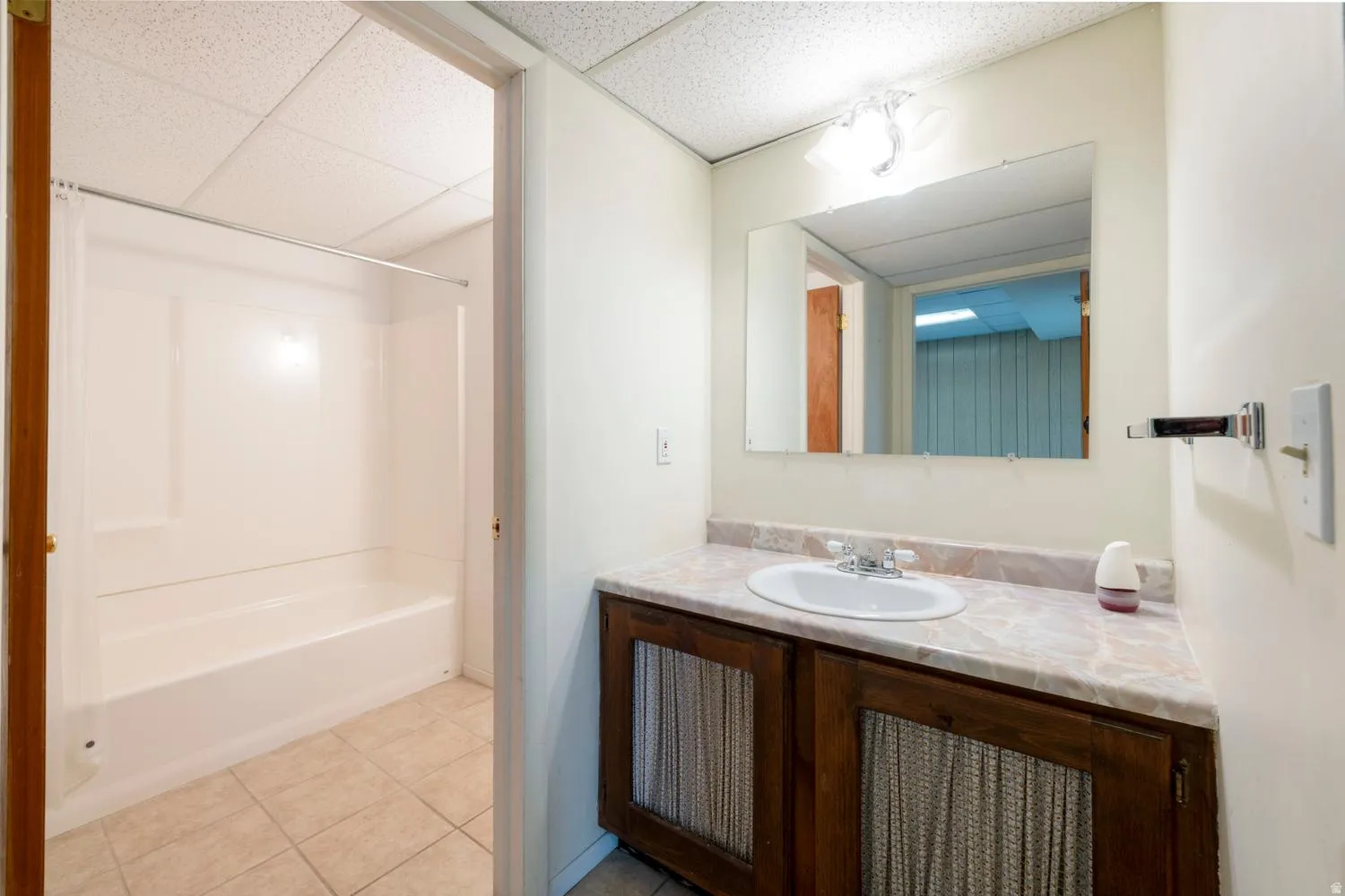 White integrated shower and tub unit, tile flooring, vanity with integrated sink, wood-finish cabinetry, and wall-mounted mirror
