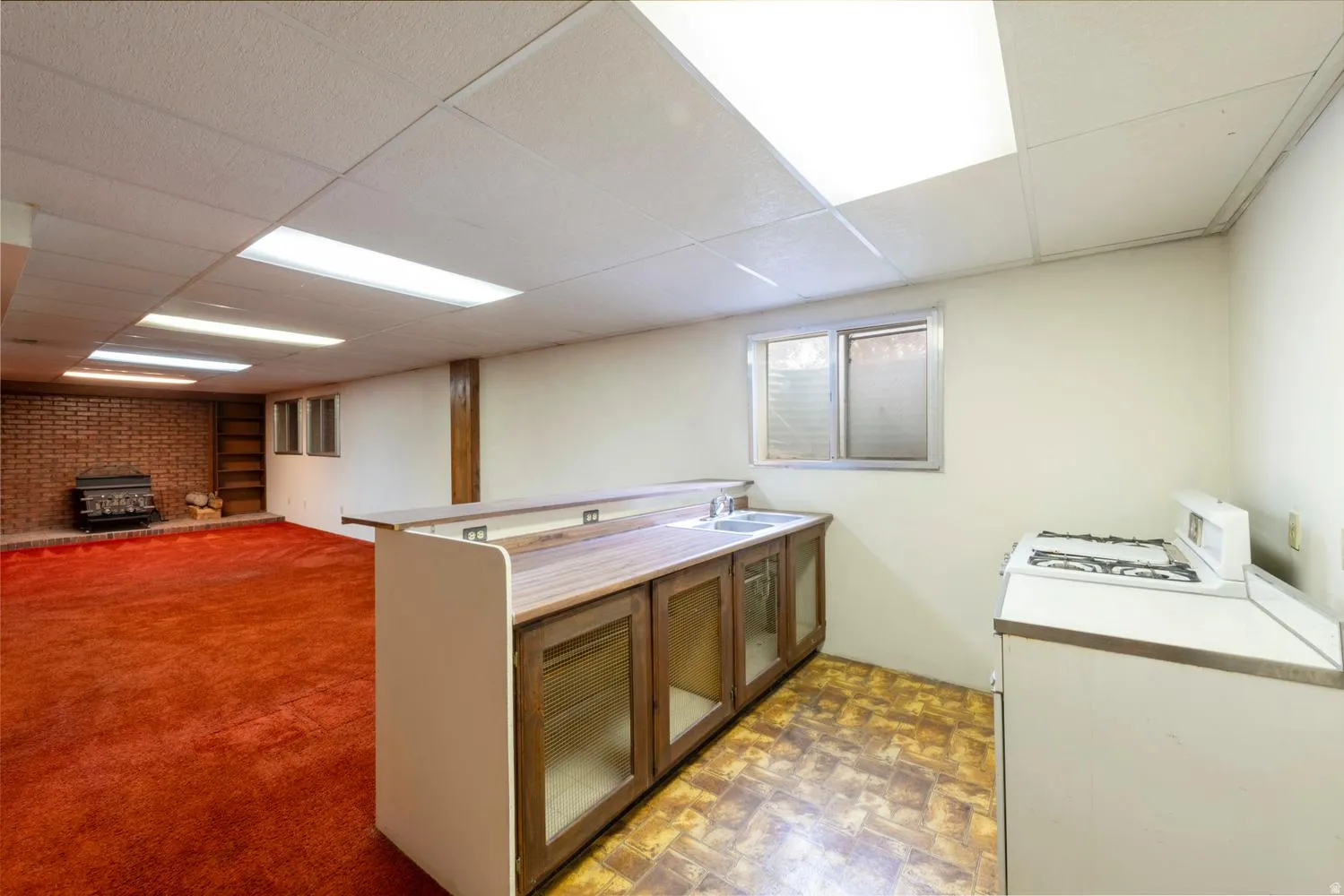 Expansive finished lower level featuring a brick-clad wood-burning fireplace, built-in shelving, wood-finish bar with integrated sink, and drop ceiling with fluorescent lighting