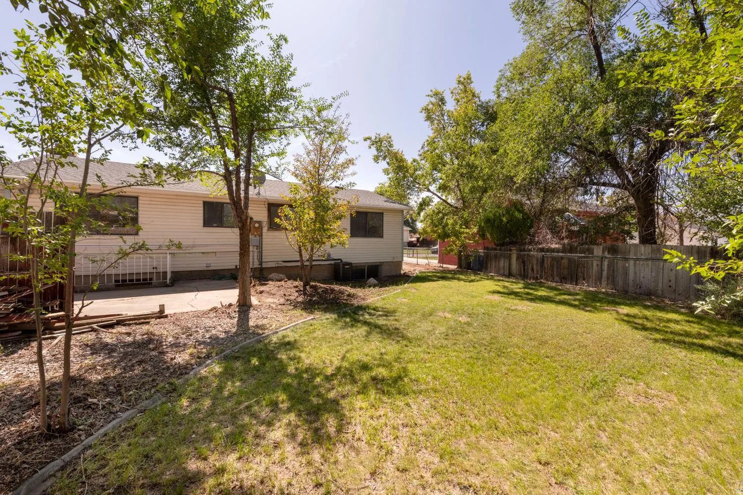 Expansive backyard featuring a lush lawn, mature trees, concrete patio, and a wood fence
