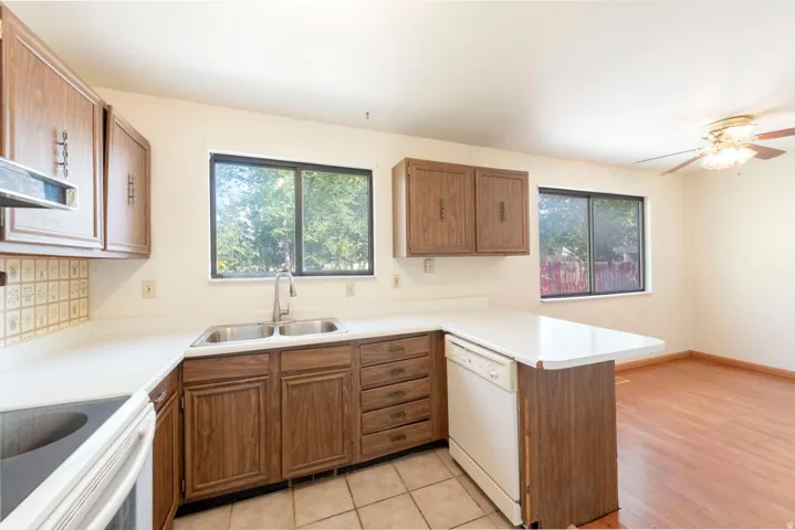 Kitchen featuring wood-finish cabinetry, a double basin stainless steel sink, tile backsplash, and an integrated dishwasher