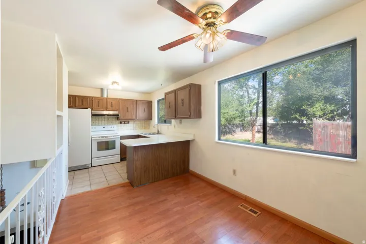 Wood-finish flooring, full kitchen with white appliances, built-in shelving, ceiling fan with light fixture, and a large window overlooking the exterior