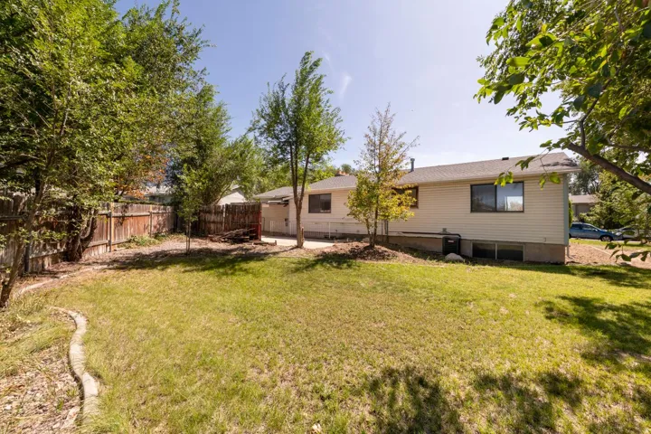 Expansive rear yard featuring green lawn, mature trees, and a wooden perimeter fence